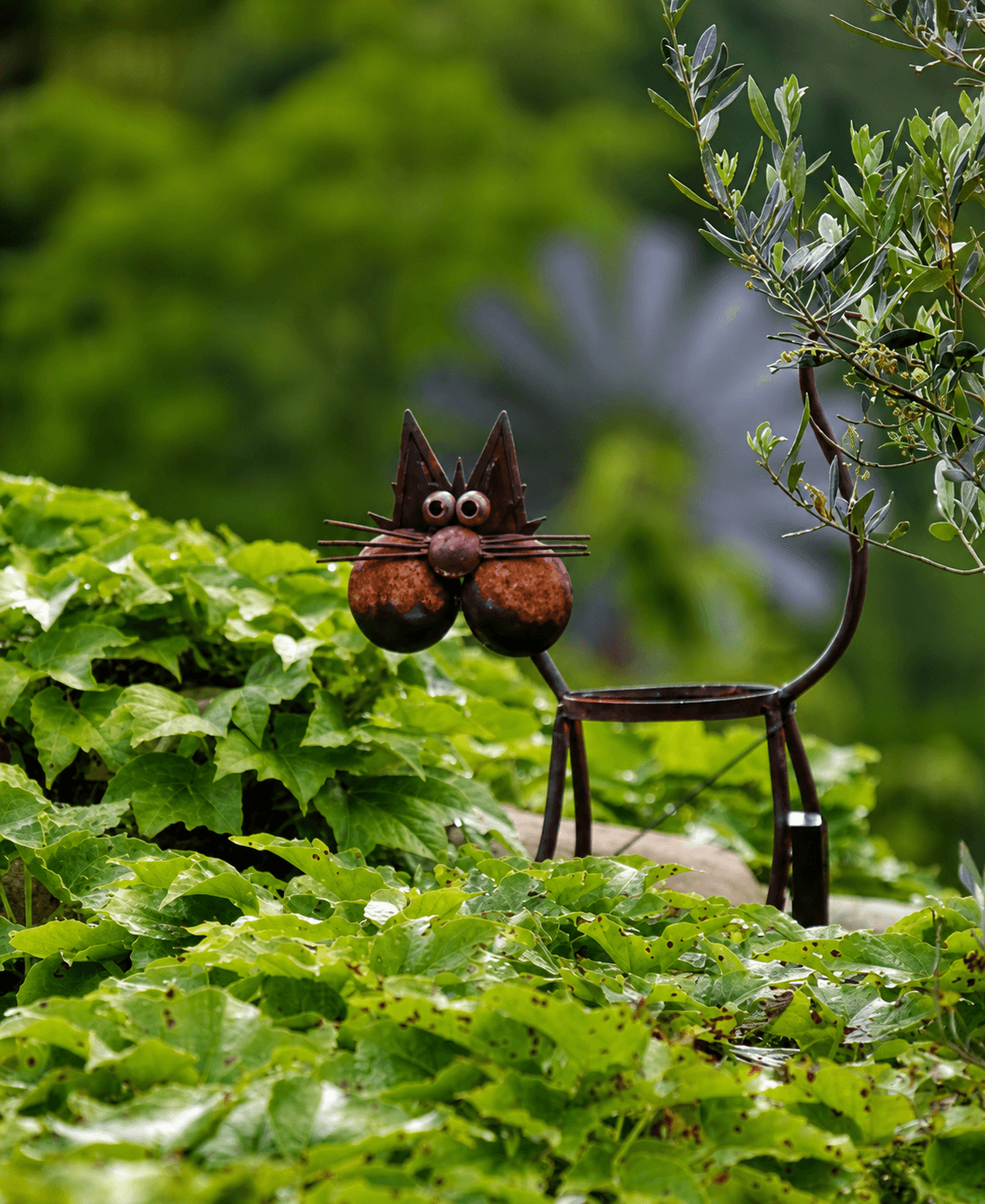 Une sculpture de chat en métal parmi les feuilles du jardin.