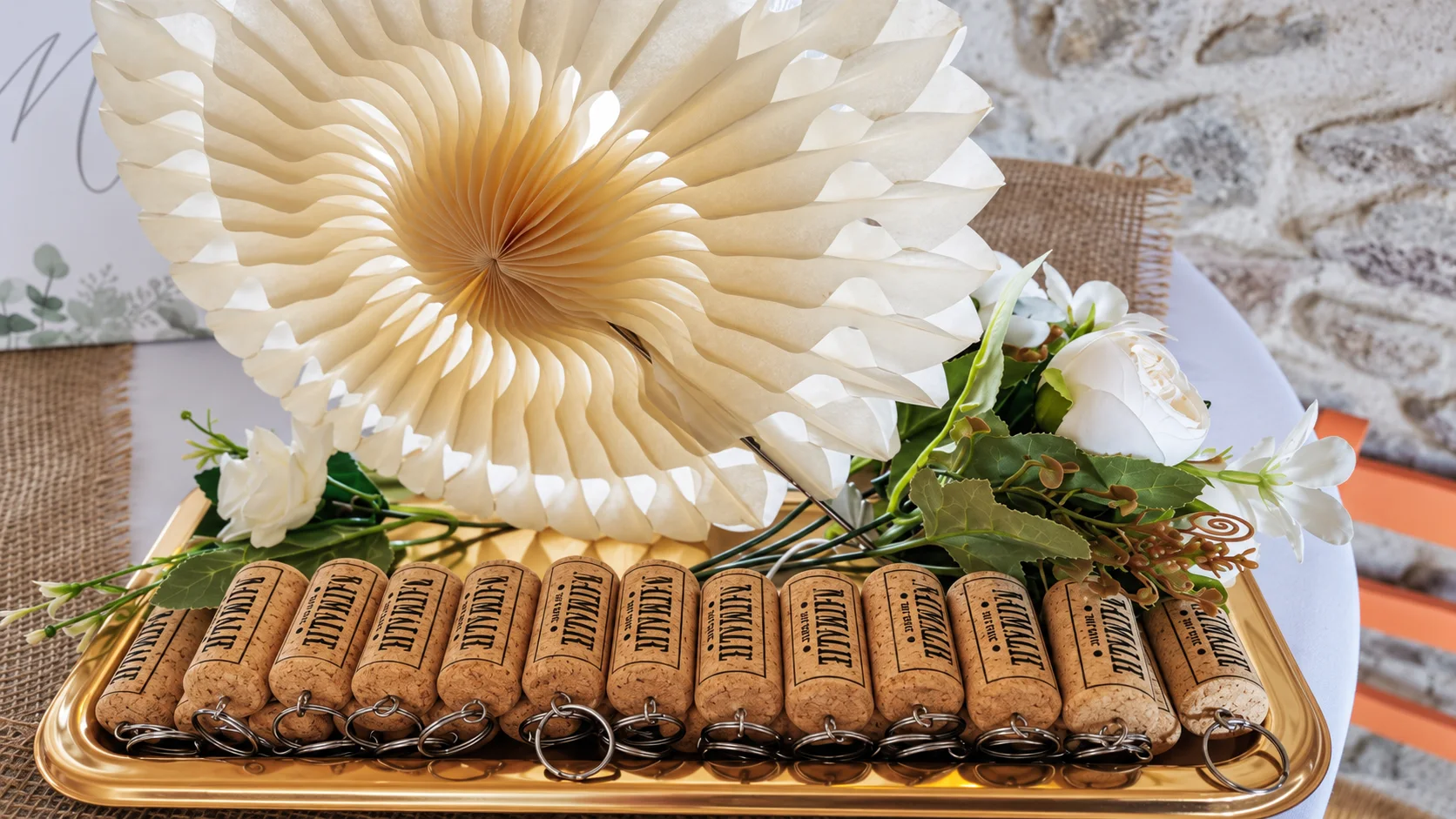 Porte-clés en bouchon disposés sur un plateau avec des fleurs blanches et une rosace en papier