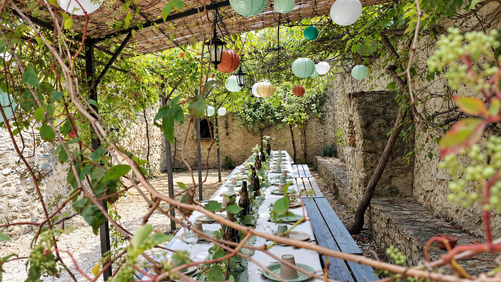Longue table dressée avec des bancs sous la treille et des lanternes en papier dans la cour du Mas d'Eylieux