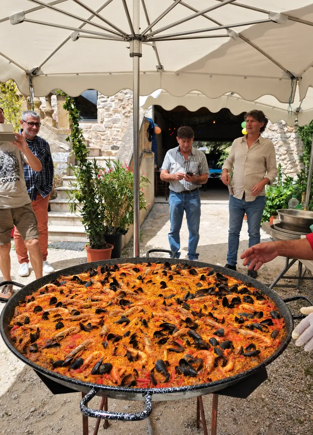 Paella garniert unter den Sonnenschirmen mit Gästen im Innenhof des Mas