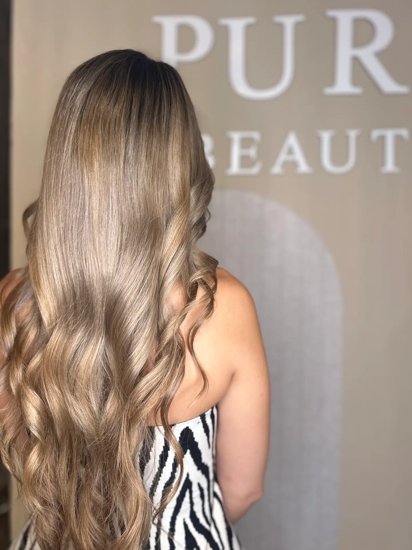 Langes blondes Haar mit Wellen vor dem Schild des Pure Beauté Salons